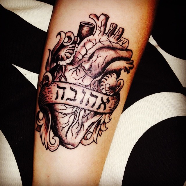 Detailed anatomic heart with Arabic banner lettering arm tattoo