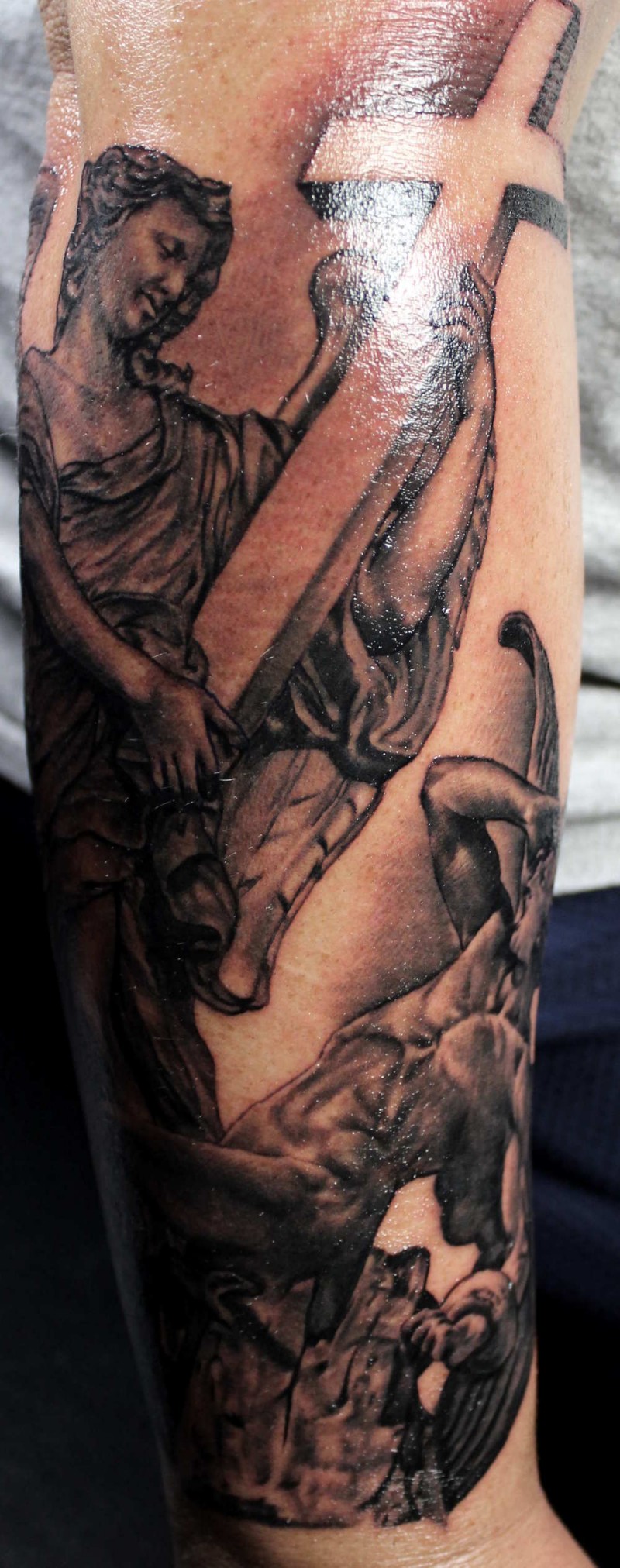 Dramatic religious themed black ink forearm tattoo on angels with cross