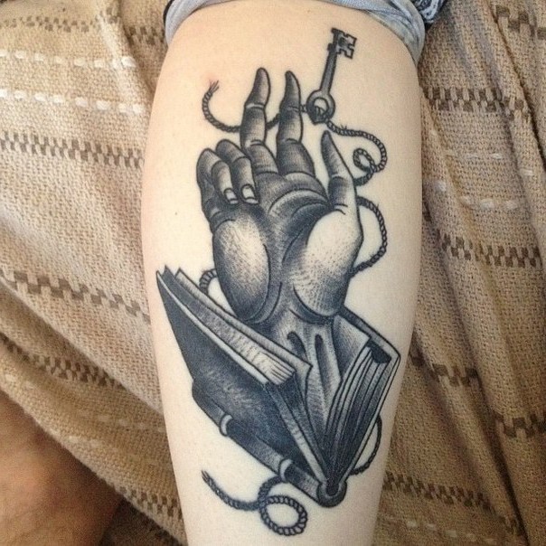 Engraving style black ink leg tattoo of human hand in book with key