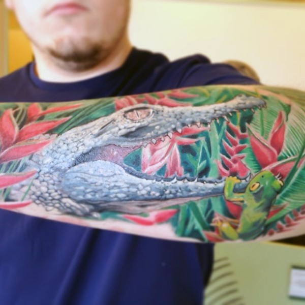 Fantastic natural looking colored little alligator with frog tattoo on arm