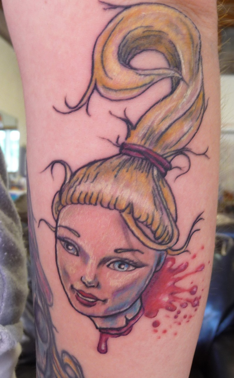 Funny cartoon like severed head of Barby doll tattoo on forearm