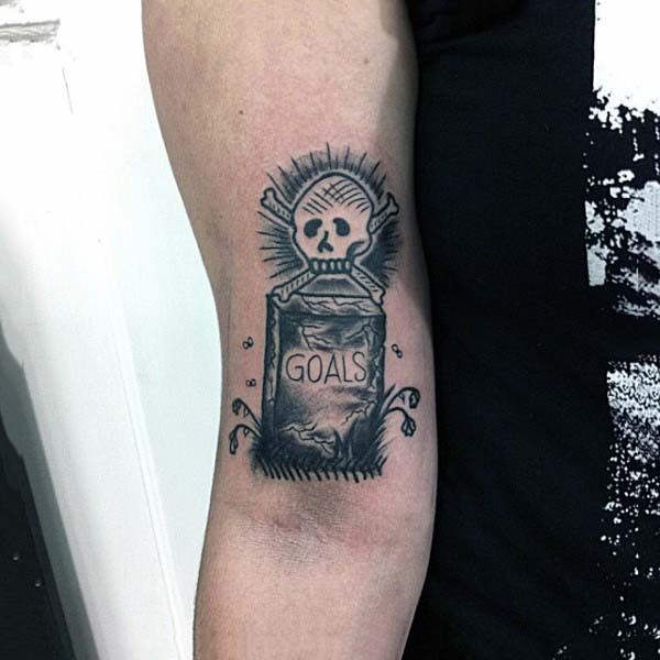 Tatuaje en el brazo, lápida con escrito y calavera, colores negro blanco
