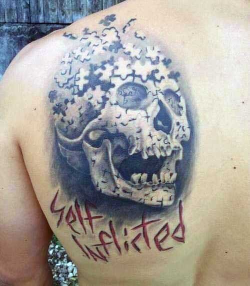 Funny looking black ink shoulder tattoo of puzzle picture stylized with human skull and lettering
