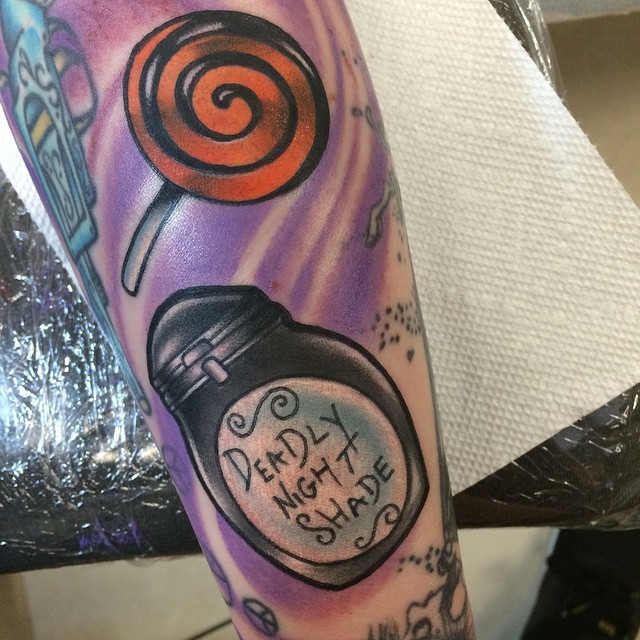 Lustig bemaltes und gefärbtes  Lollipop Tattoo am Arm mit Glas und Schriftzug