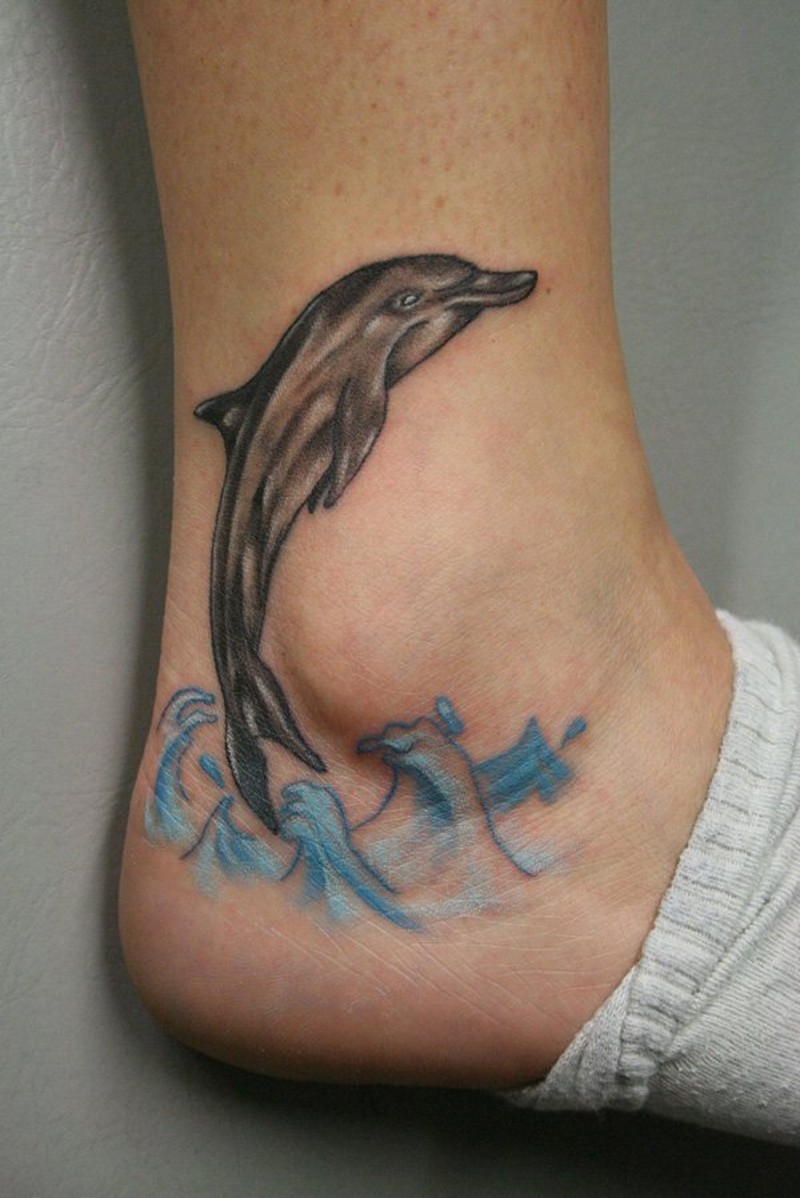 Funny painted little dolphin in waves tattoo on ankle