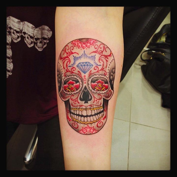 Funny smiling multicolored skull in Mexican style forearm tattoo