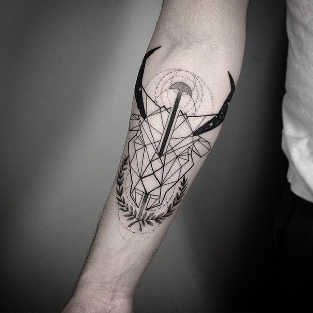 Geometrical style black ink forearm tattoo of goats head with leaves