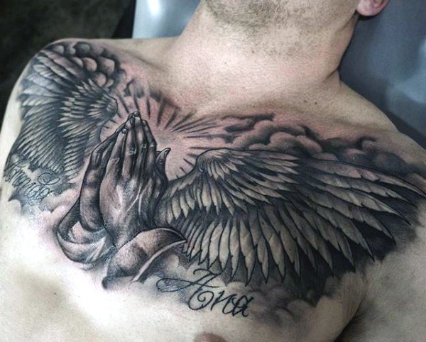 Tatuaje muy espectacular tratando el tema religioso las manos rezando y las alas en el pecho