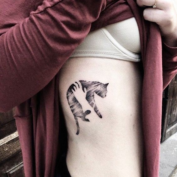 Gorgeous looking black ink side tattoo of hands holding cat