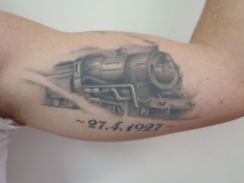 Tinta gris en movimiento antiguo tatuaje conmemorativo de tren humeante en bíceps con fecha