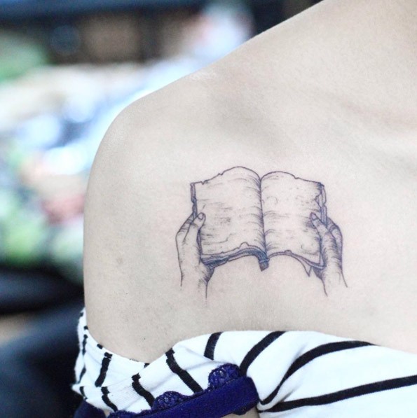 Tatuaje en el hombro, dibujo pequeño negro blanco de 
 manos con libro