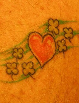 el tatuaje sencillo de un corazon rojo con unos treboles