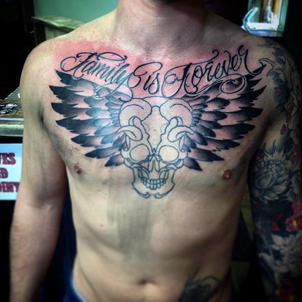 Gehörnter Schädel mit großen Federflügeln und Schriftzug Tattoo an der Brust