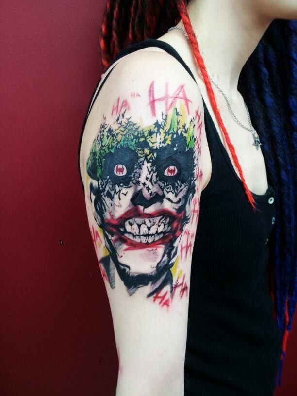 Horror movie like smiling Joker tattoo on shoulder with lettering