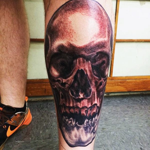 Horror style dark colored detailed human skull tattoo on calf
