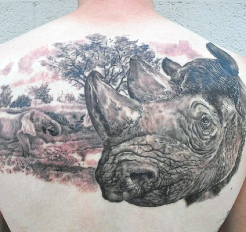 Huge detailed colored rhino head tattoo on upper back combined with elephant in wild life