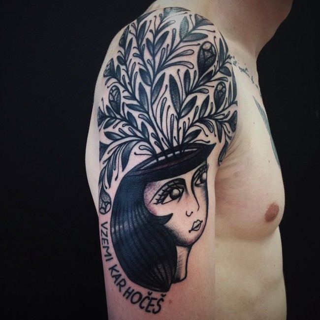 Illustrative style black ink shoulder tattoo of woman with plants and lettering