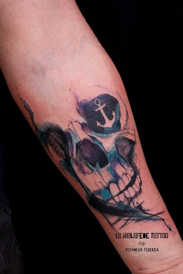 Illustrative style colored forearm tattoo of human skull stylized with anchor