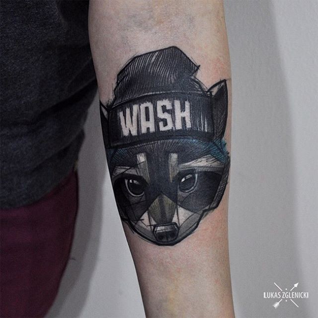 Illustrative style colored forearm tattoo of raccoon head with lettering
