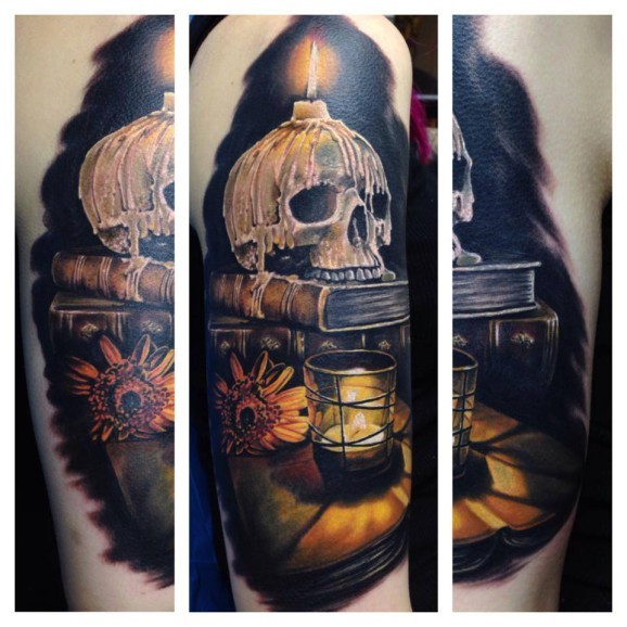 illustrative style colored shoulder tattoo of human skull with candle, book and flower