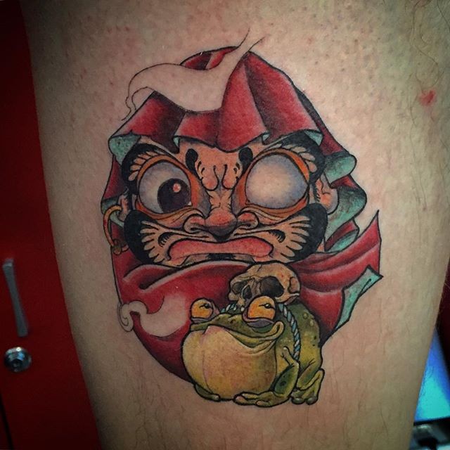 Illustrative style colored thigh tattoo of daruma doll with frog