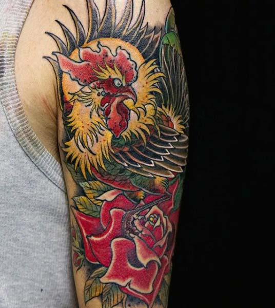 Tatuaje en el brazo, gallo abigarrado en la rosa roja