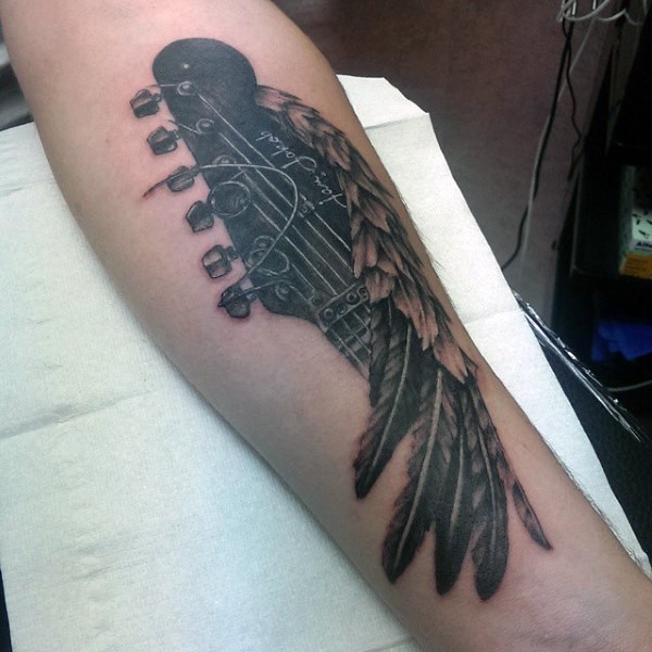 Tatuaje en el antebrazo, parte de guitarra con plumas, dibujo negro blanco