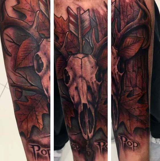 Tatuaje en el brazo, cráneo de animal con flecha en hojas otoñales