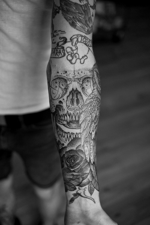 Interesting-designed gray-ink skull with wing and rose tattoo sleeve on forearm