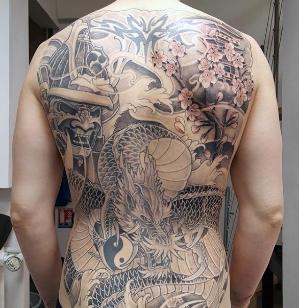 Japanese style black ink whole back tattoo of dragon with mask and blooming tree