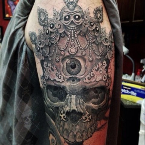 Large illustrative style shoulder tattoo of human skull with crown and eye