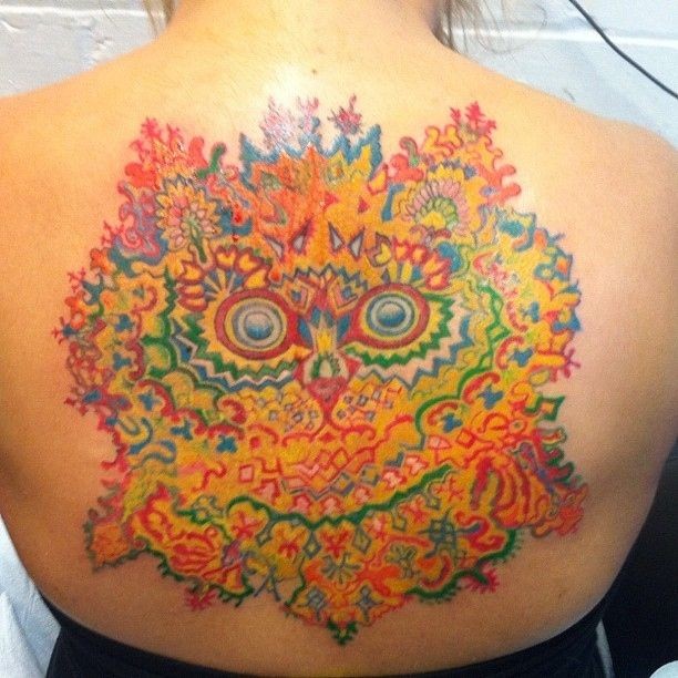 Large multicolored upper back tattoo of flowers and cat like face
