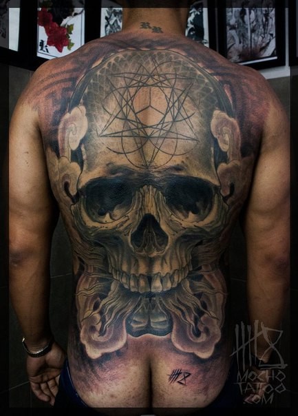 Large mystical looking whole back tattoo of big skull with ornaments and smoke
