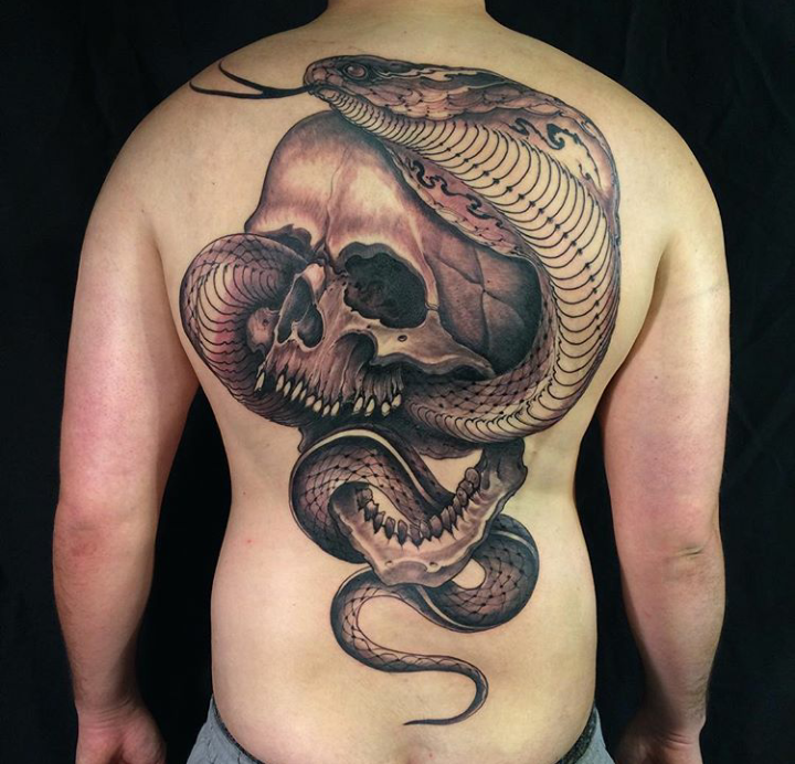 Large very detailed whole back tattoo of human skull with large snake
