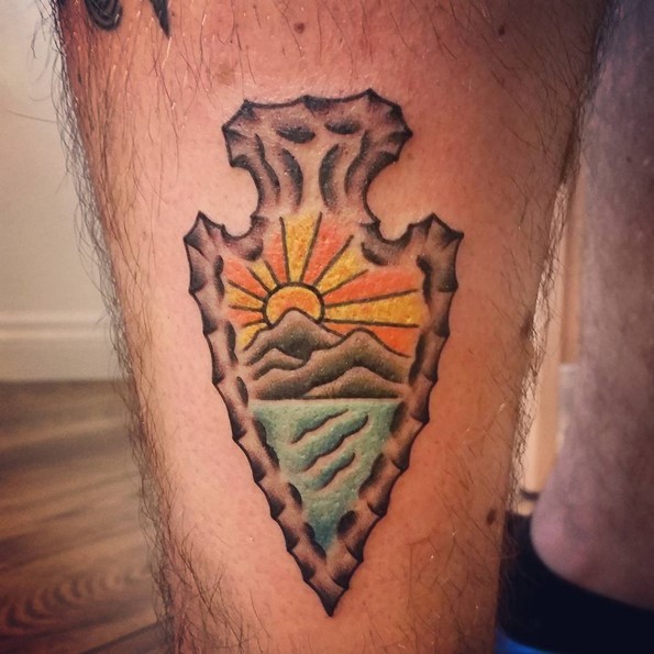 Little 3D like colored ancient tribal weapon tattoo on leg stylized with sun and mountains