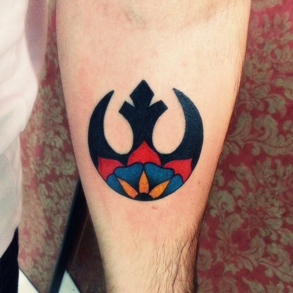 Little black ink Rebel Alliance emblem tattoo on forearm stylized with colored flower