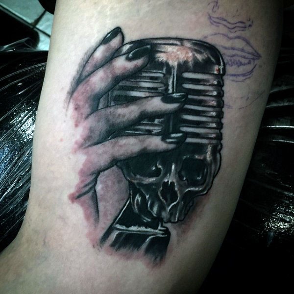Kleines schwarzes unvollendetes Tattoo mit Mikrofon in der Form vom Schädel  am Arm