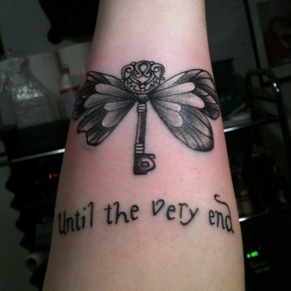Little butterfly shaped key with wings tattoo on forearm with &quotUntil the very end" lettering