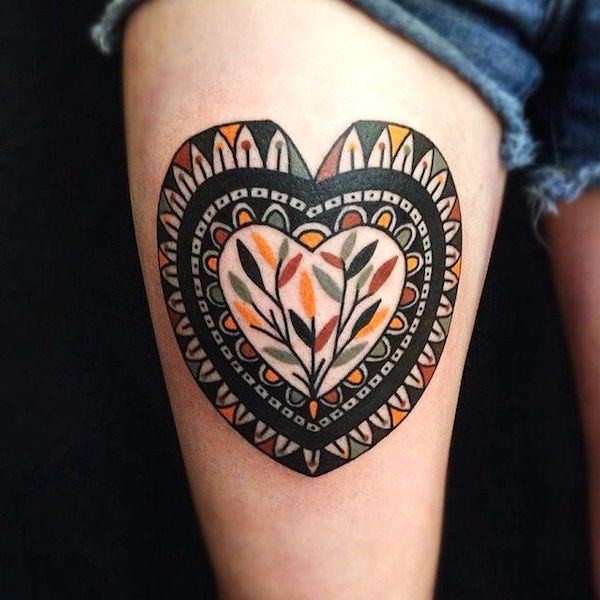 Little colored heart shaped tattoo on thigh stylized with tribal ornaments and tree