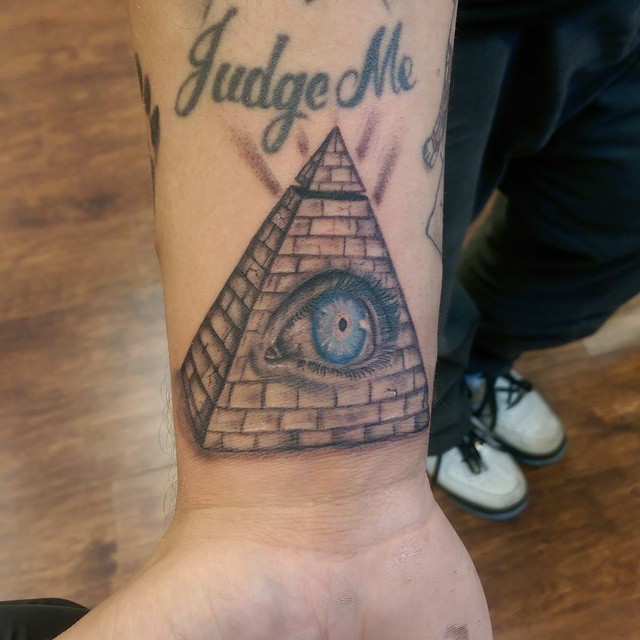 Tatuaje en la muñeca,
 pirámide con ojo azul y inscripción