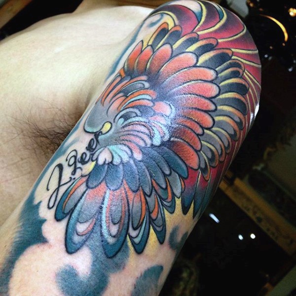 Little multicolored fantasy wing with lettering tattoo on arm