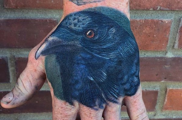 Little wise looking colored crow tattoo on hand