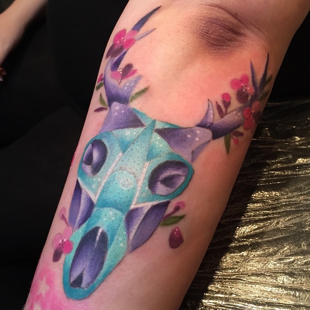 Magnificent colorful alien like animal skull tattoo on forearm stylized with flowers