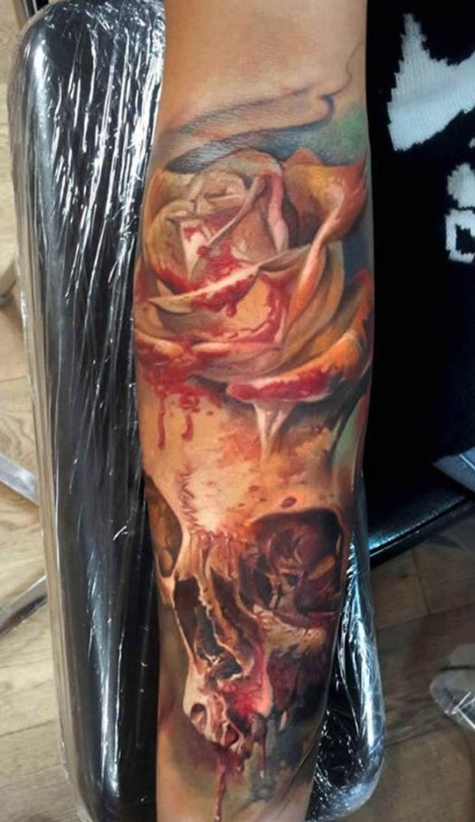 Magnificent multicolored bloody rose tattoo on forearm combined with human skull