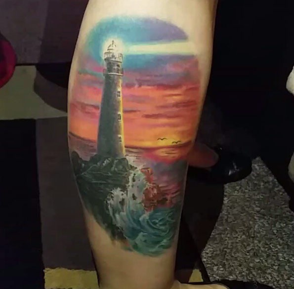 Marvelous multicolored lighthouse tattoo on leg with beautiful sunset