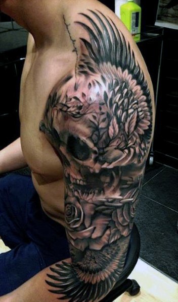 Tatuaje en el brazo, cráneo enorme con alas de águila y flores