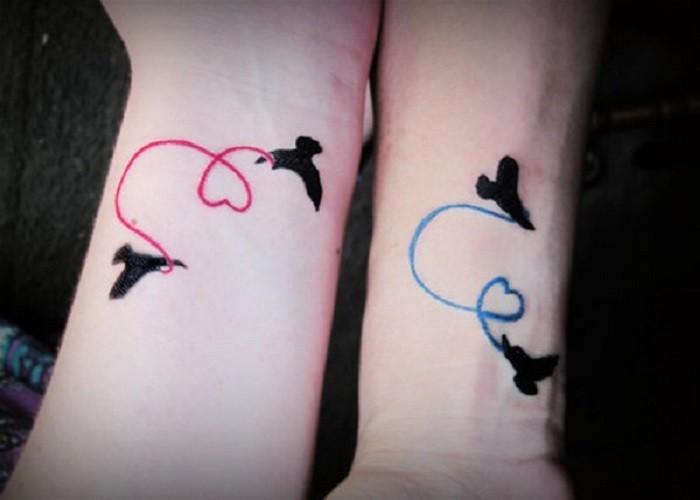 Tatuajes en las muñecas, aves negras con cintas de colores rosa y azul