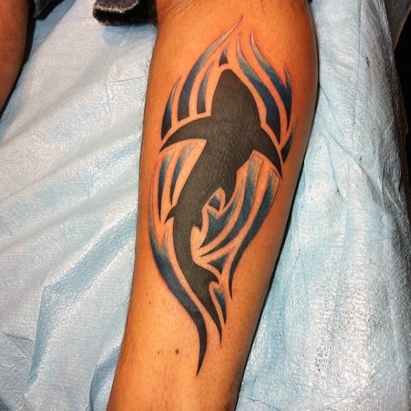 Medium size colored black shark tattoo on leg stylized with blue waves