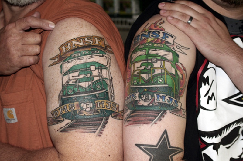 Memorial style colored upper arm tattoo of trains with lettering