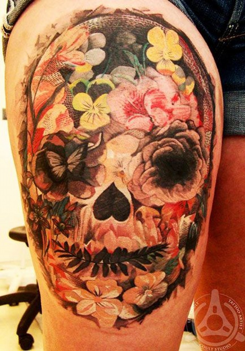 Tatuaje en el muslo, 
cráneo abigarrado decorado con flores